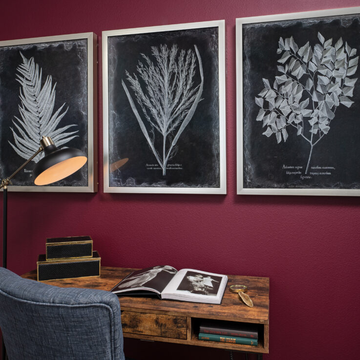 Three black and white paintings of leaves on a purple wall