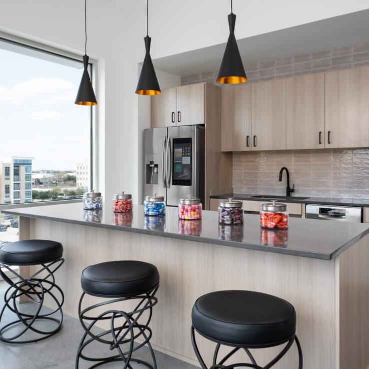 Kitchen area with light brown cabinets, black countertops, and black stools