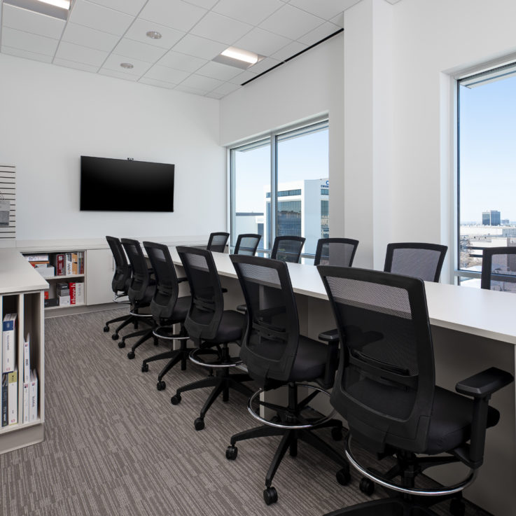 Shared work area with white countertop, black office chairs, and a flatscreen television