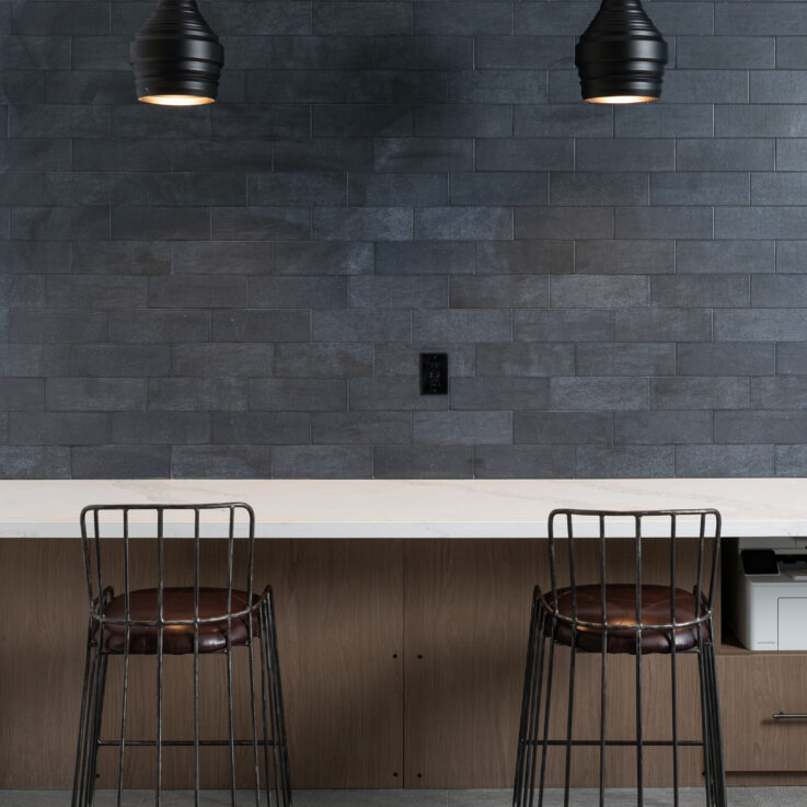 Two brown barstools, a white countertop, and a dark blue tiled wall