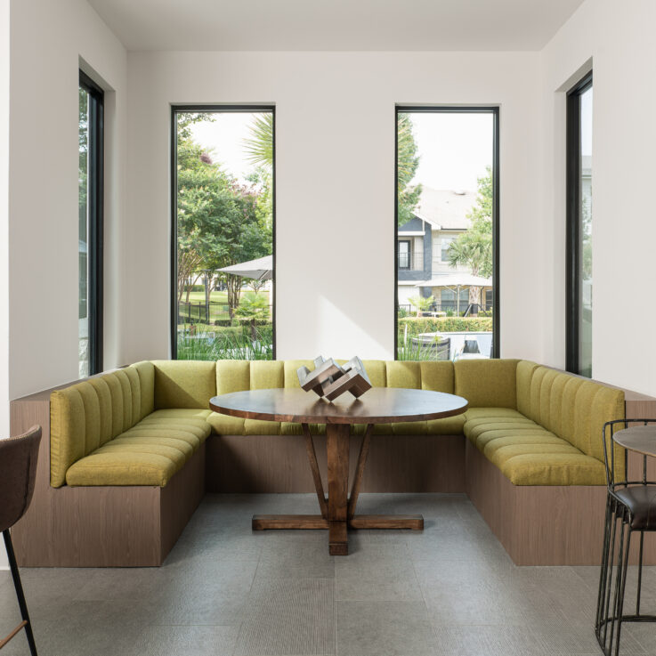 Three sided brown and green couch around a circular wooden table