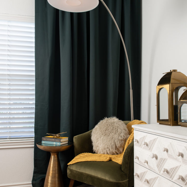 White dresser next to a green chair and dark green curtains