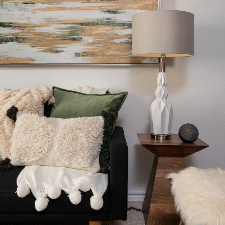 Black couch with green and white pillows and an endtable