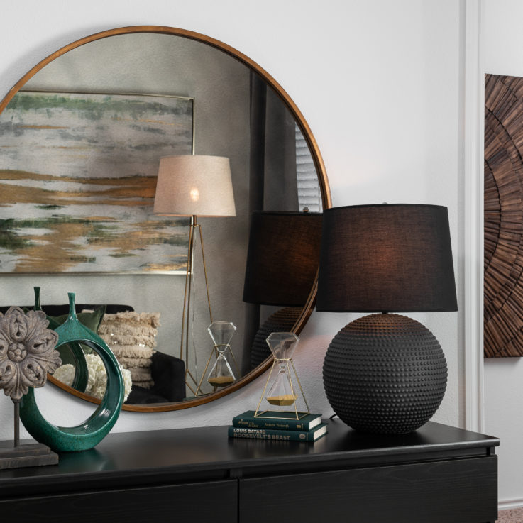 Black dresser with a lamp and a circular wall mirror