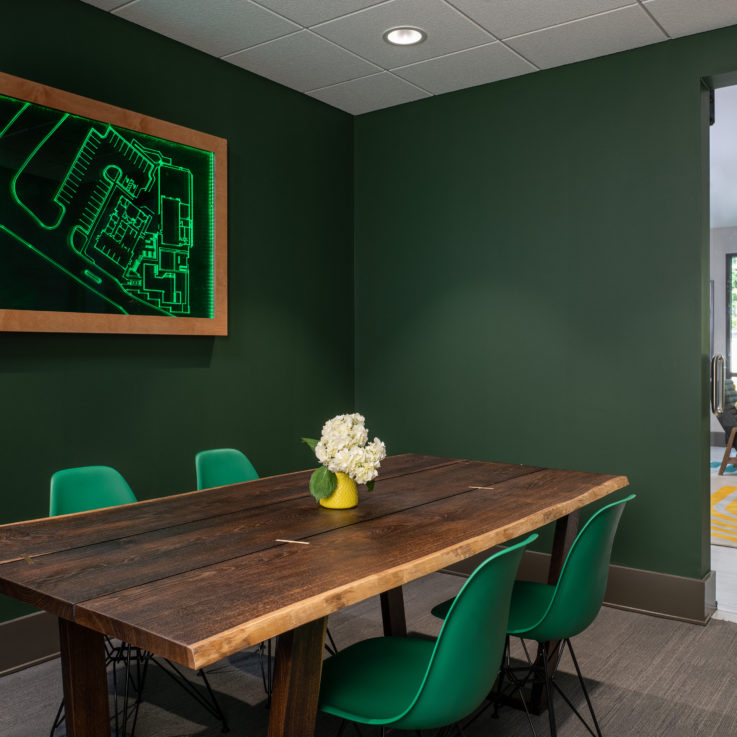 Wooden table with four plastic green chairs and dark green walls