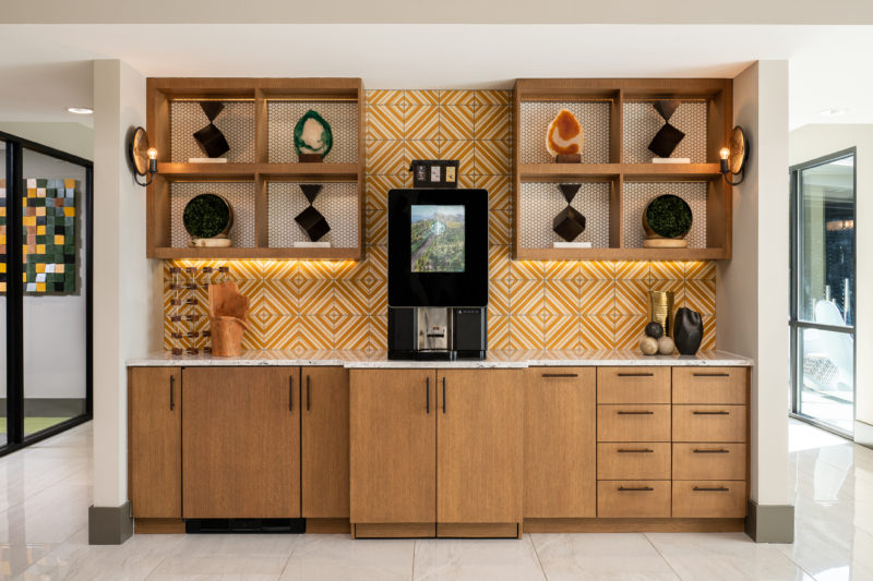 Kitchen area with wooden cabinets, an orange and white tiled wall, and a coffee maker