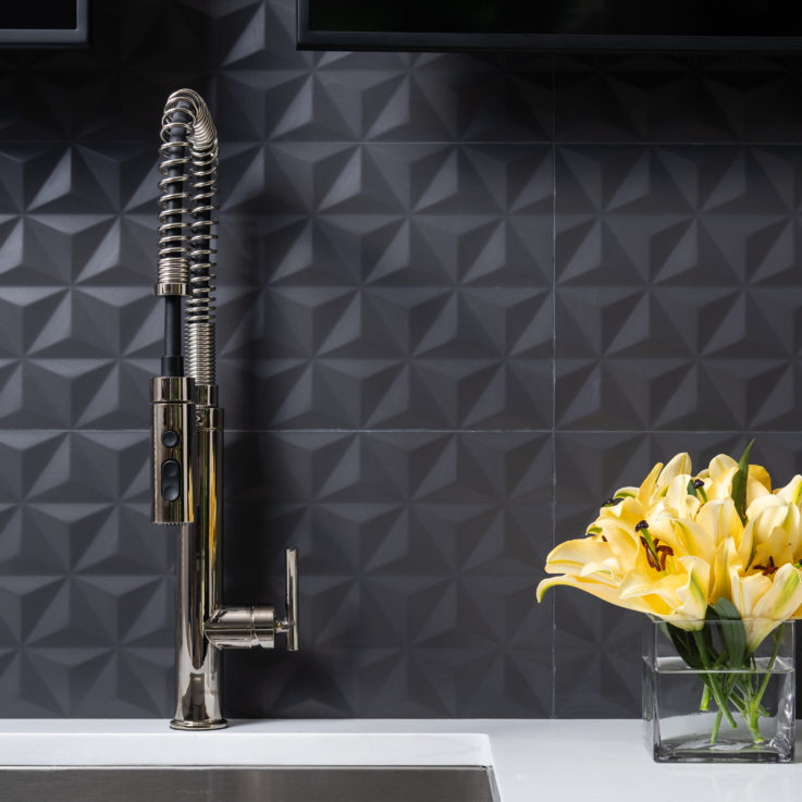 Faucet on a white countertop with black tiles on the wall