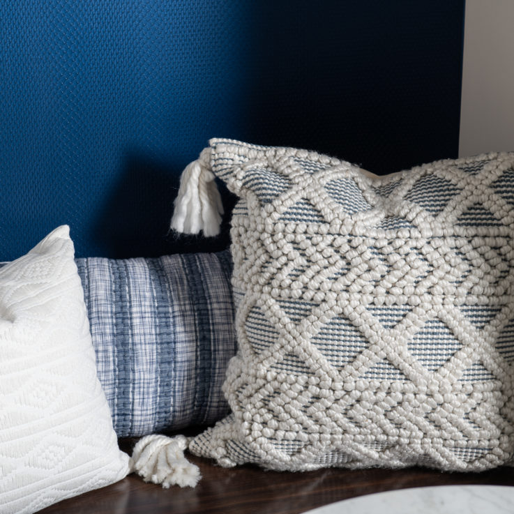 Three blue and white pillows on a wooden bench in front of a dark blue wall