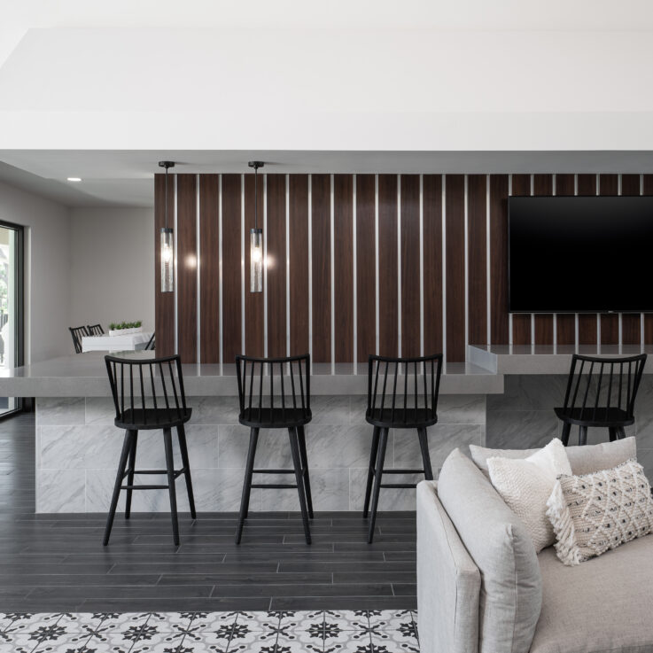 Gray, granite bar with black chairs against a wood paneled wall