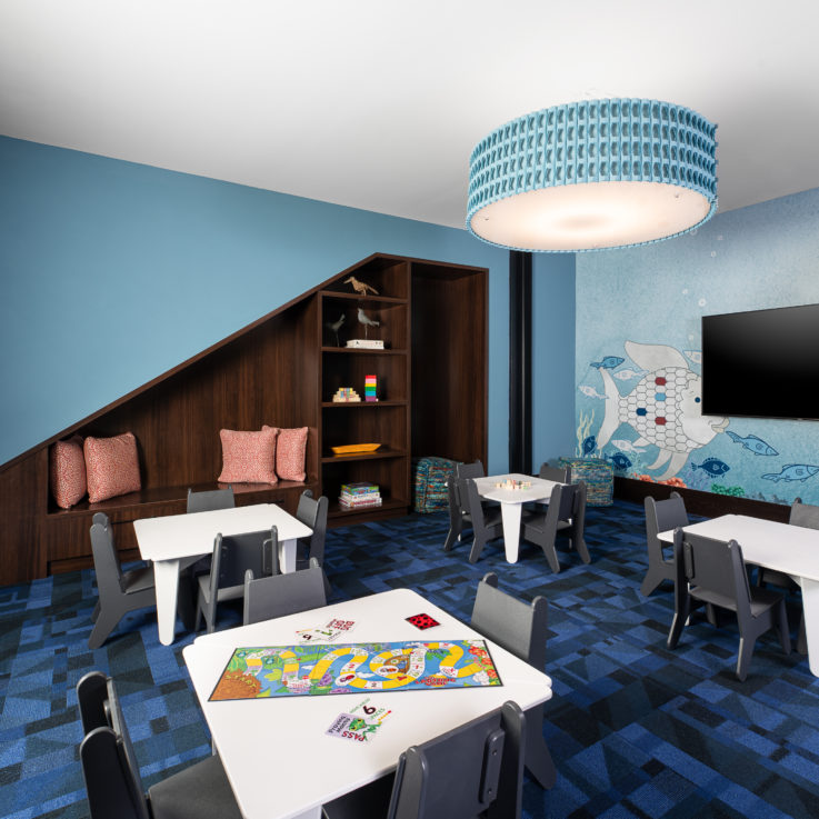 Childrens playroom with white tables, gray chairs, and flatscreen television