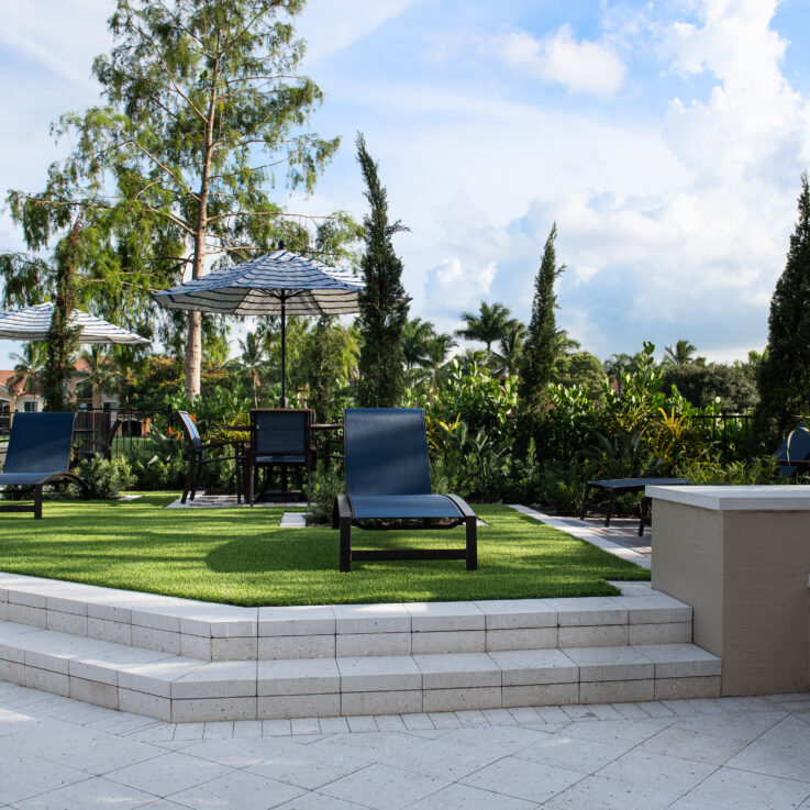 Dark blue beach chairs on grass with tables, chairs, and umbrellas behind them