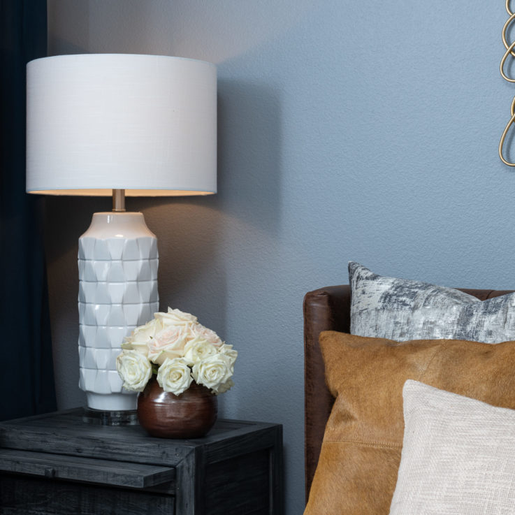Bedside table with a light blue lamp and a pot with white roses