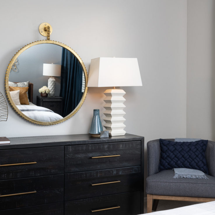 Black dresser with a white lamp below a circular mirror