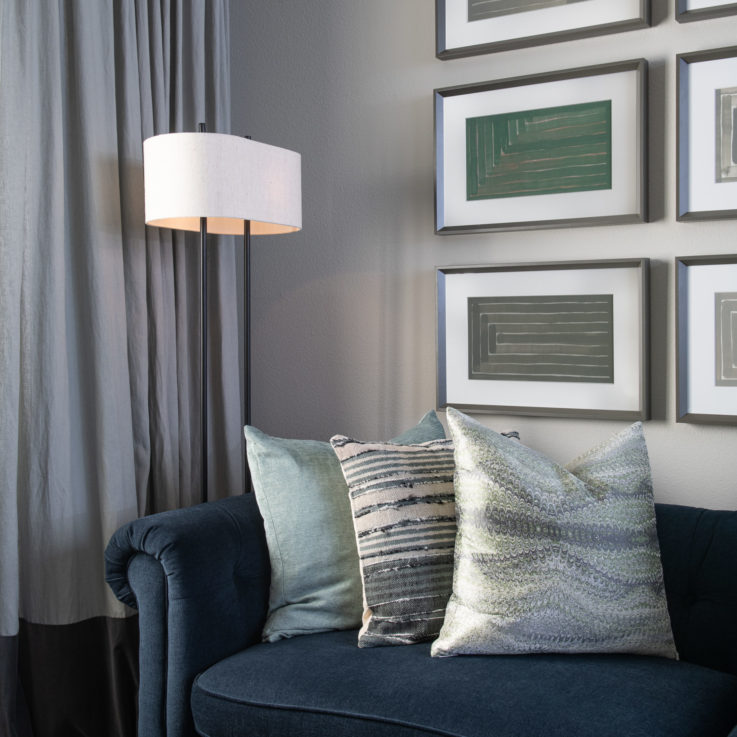 Dark blue couch with three pillows next to a standing lamp