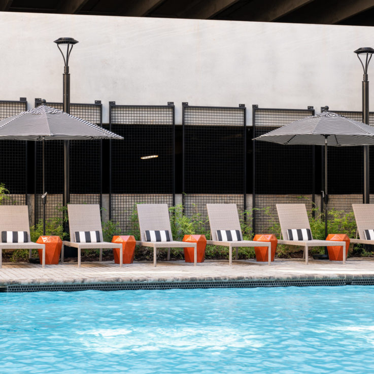 Beach chairs near an outdoor pool with striped umbrellas