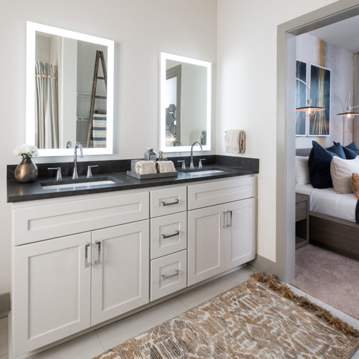 Two bathroom sinks with white cabinets and a dark countertop