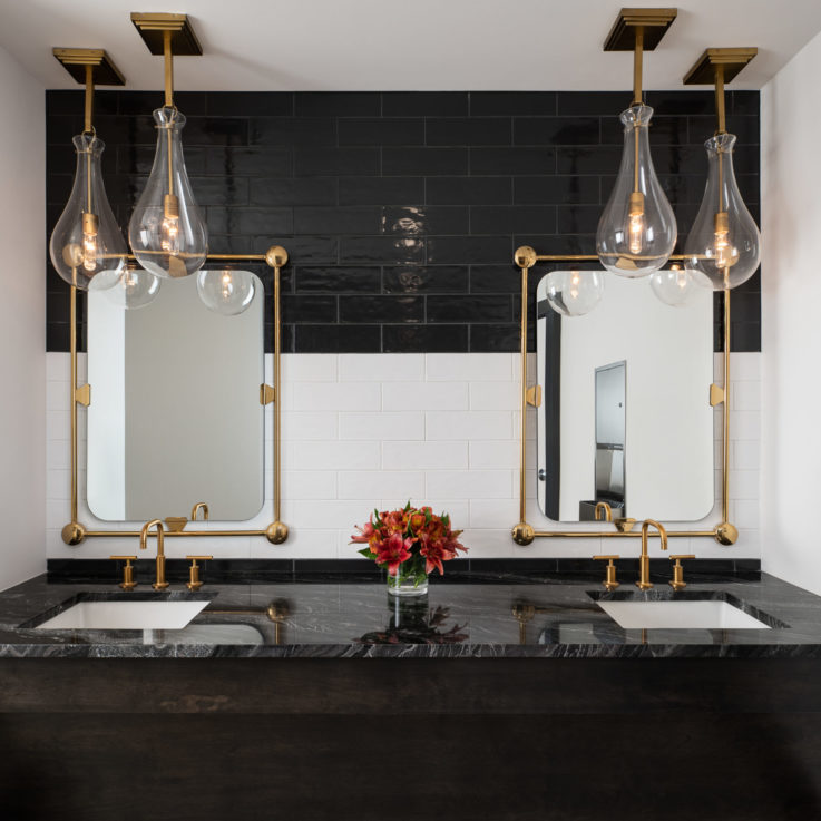 Two bathroom sinks with a dark marble countertop and brass faucets