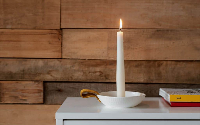 Tall white candle in saucer on dresser